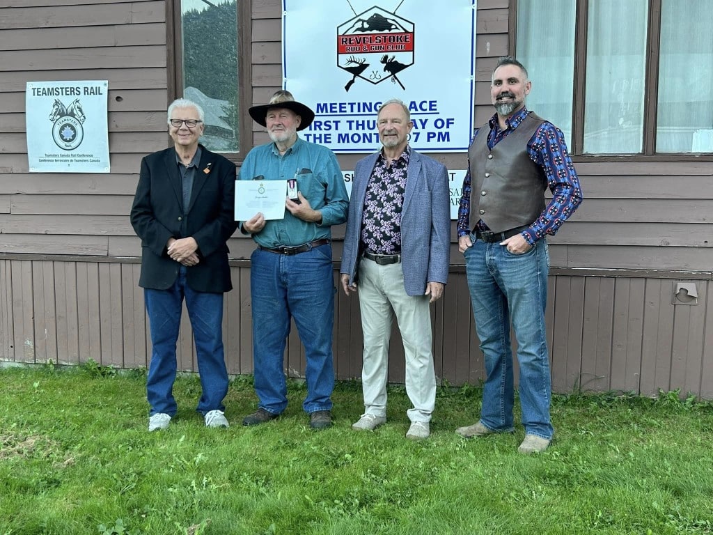 Four white men of varying ages stand in front of the Revelstoke rod and gun club building.