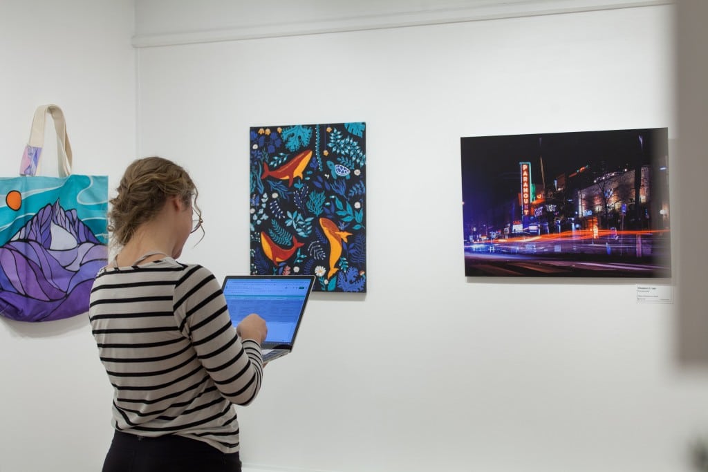 Staff standing in front of a row of paintings for the Winter Art Market