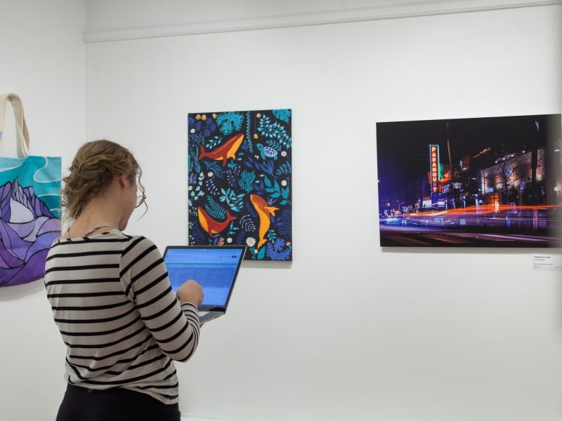 Staff standing in front of a row of paintings for the Winter Art Market
