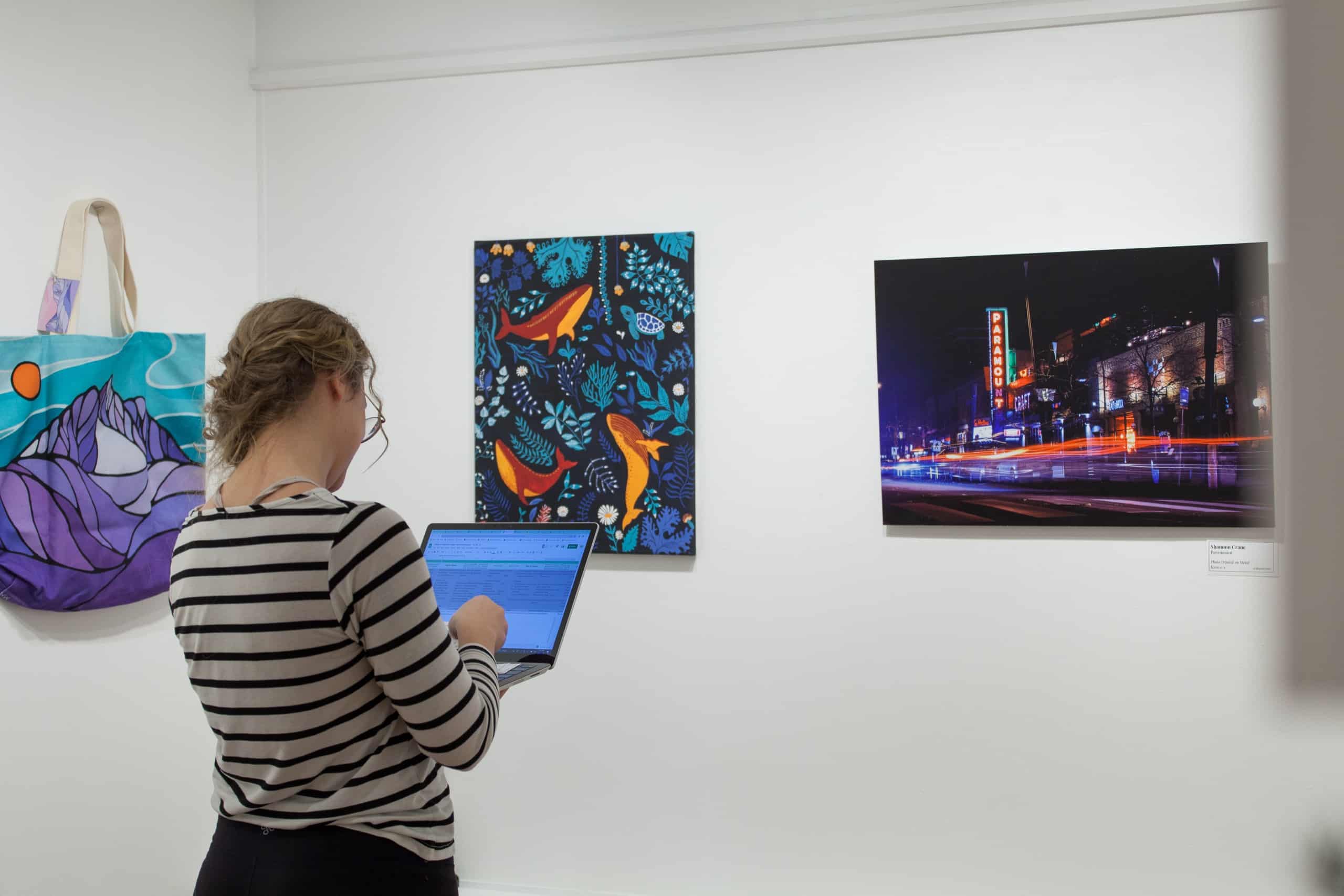 Staff standing in front of a row of paintings for the Winter Art Market