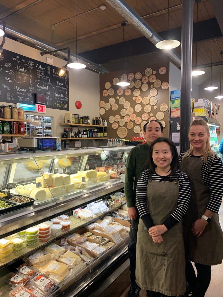 Revelstoke business Le Marche team stands to the right of their cheese cooler and smile at the camera