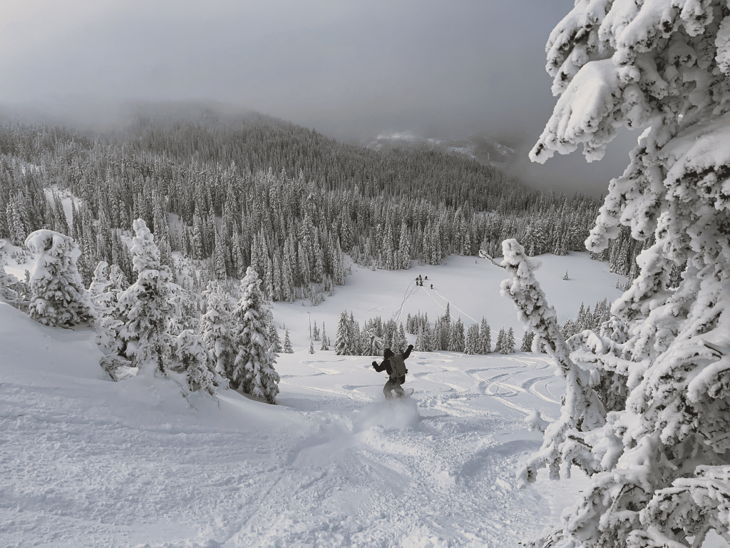 A snowboarder heading down a valley in deep, powdery snow