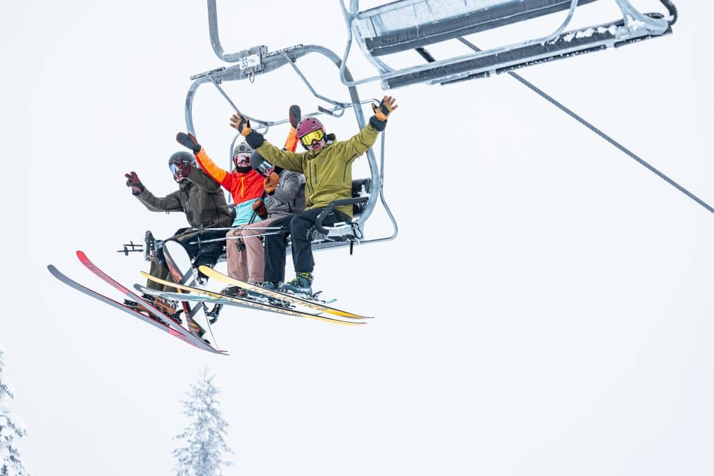 Three skiiers in winter gear sitting in a chair lift, waving at the camera as they head up Revelstoke Mountain Resort