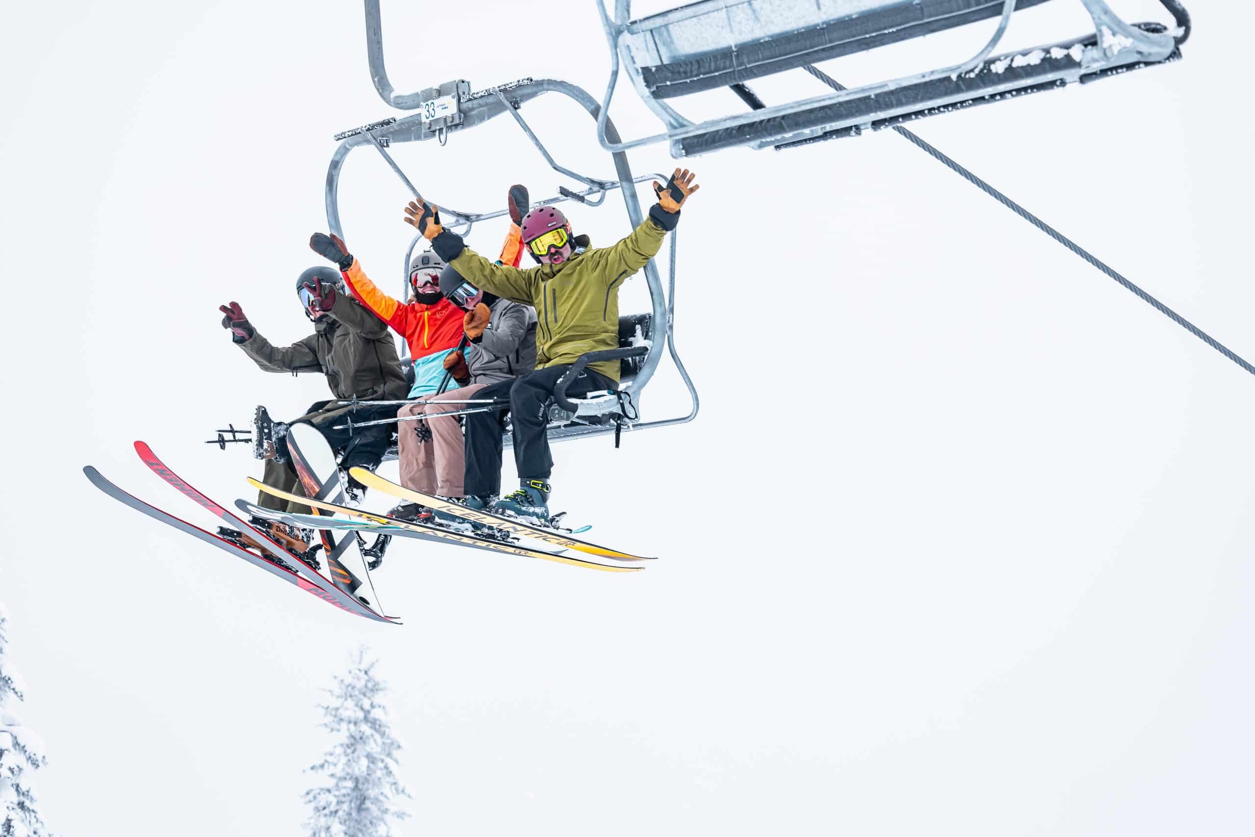 Three skiiers in winter gear sitting in a chair lift, waving at the camera as they head up Revelstoke Mountain Resort