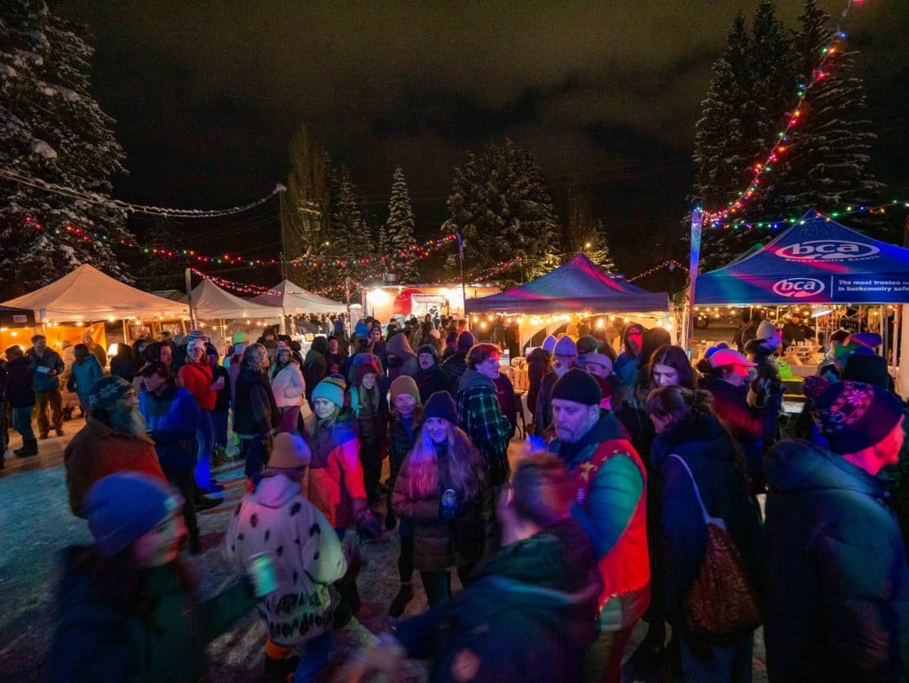 A night shot of folks at the Big Eddy Winter Market 2024 as they gather under tents to view crafts and food