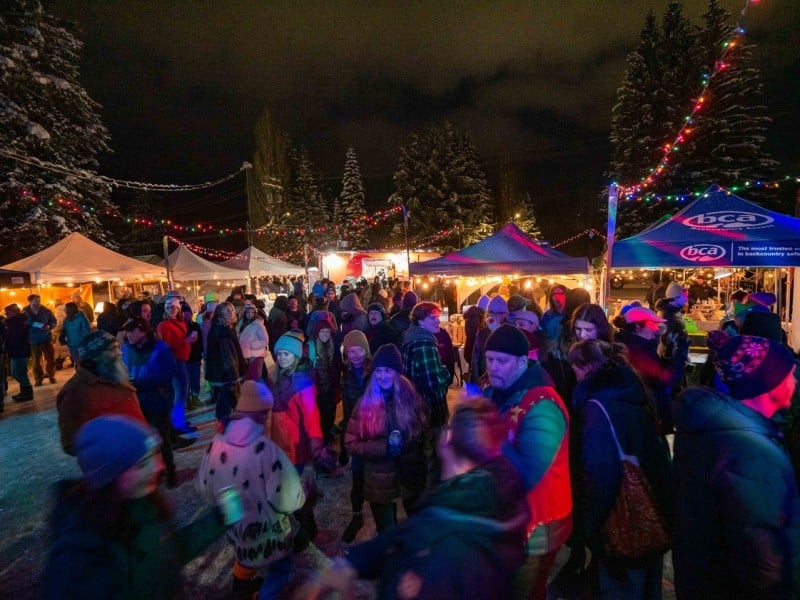 A night shot of folks at the Big Eddy Winter Market 2024 as they gather under tents to view crafts and food