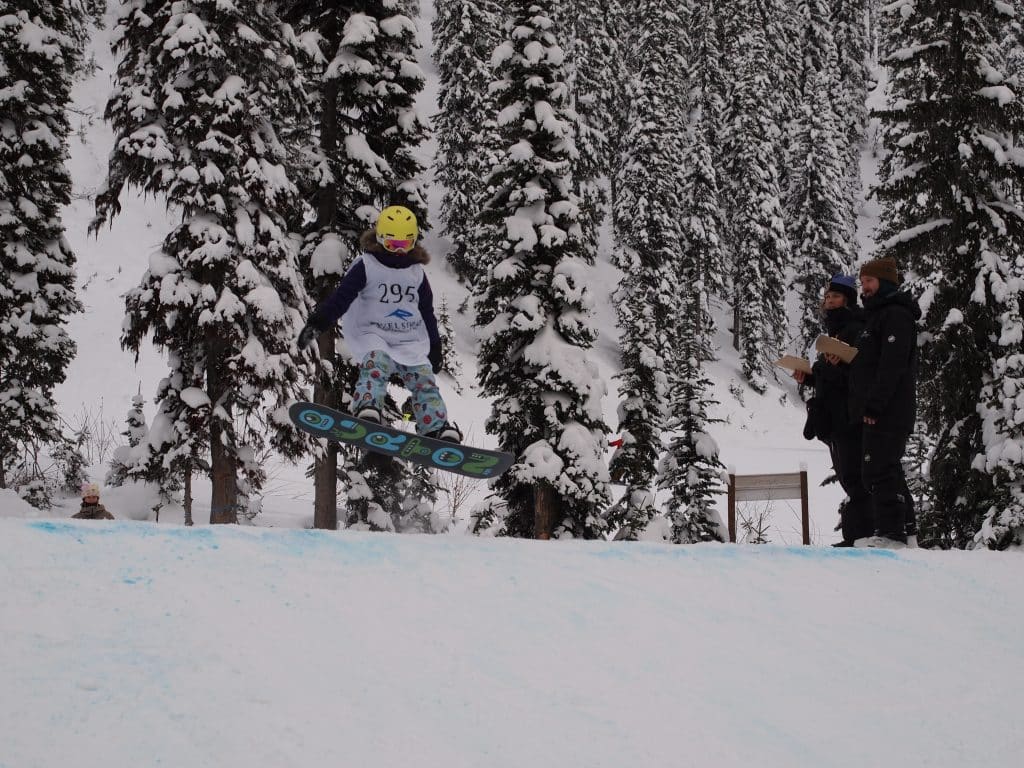Lisa Pfoster, a young snowboarder reaches for the edge of her board while taking a jump at Grom Con, hosted at Revelstoke Mountain Resort.