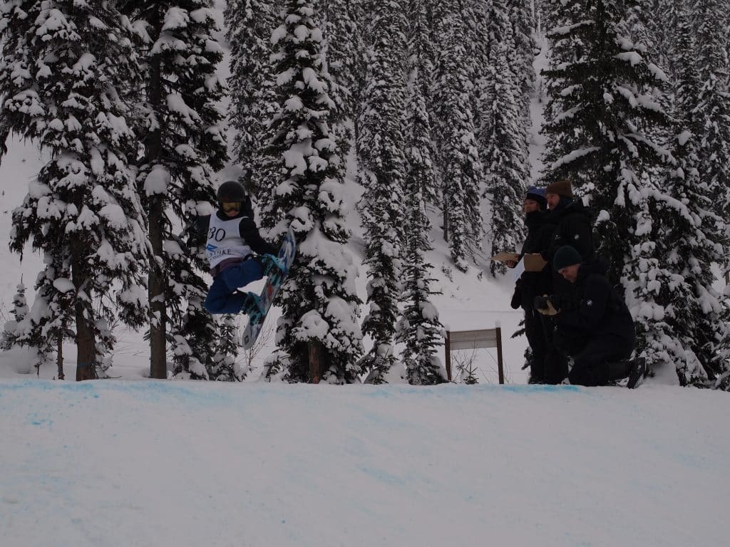 Ollie Kryskow, a young snowboarder grabs a back edge of his board coming off the kicker, a large pile of snow for jumping, at Grom Con.
