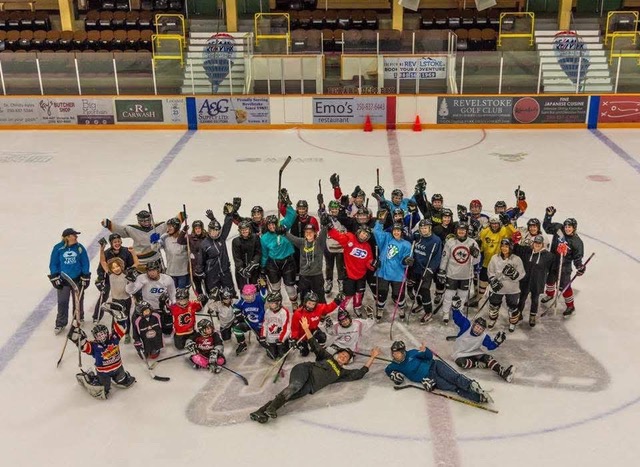 The Kodiaks Revelstoke women’s hockey league gathers on the Revelstoke Forum ice to cheer as they look up at the camera. There is roughly 30 individuals all in hockey gear on the ice.