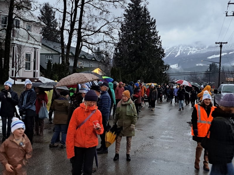 A group of walkers in rain gear and some wearing Coldest Night of the Year branded toques walk down a rainy street in Revelstoke.