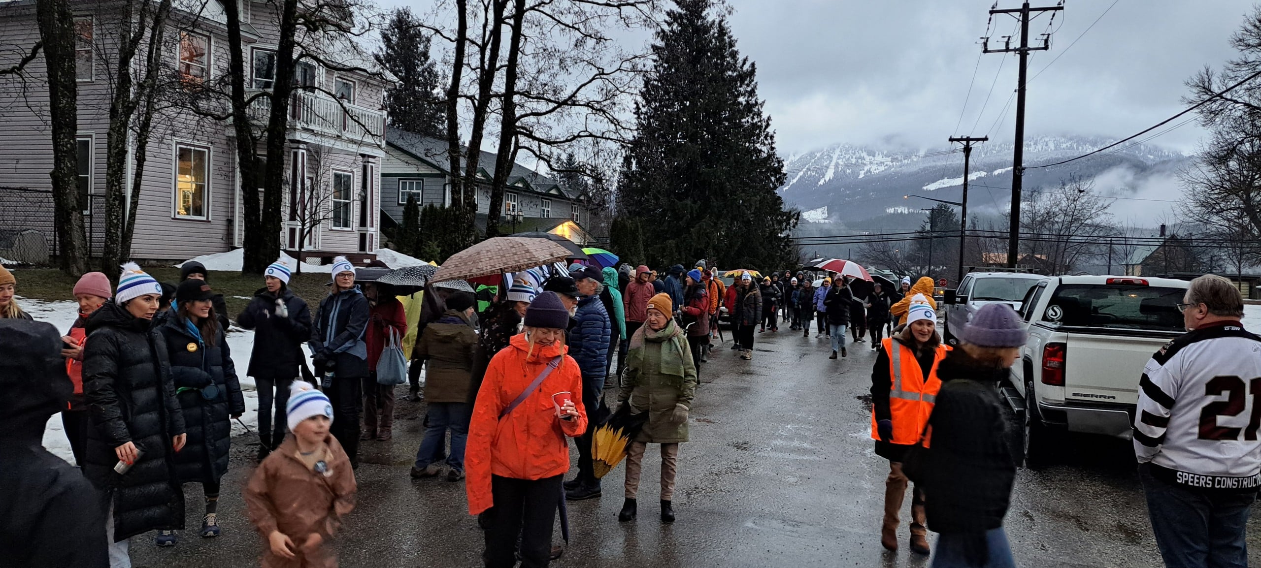 A group of walkers in rain gear and some wearing Coldest Night of the Year branded toques walk down a rainy street in Revelstoke.