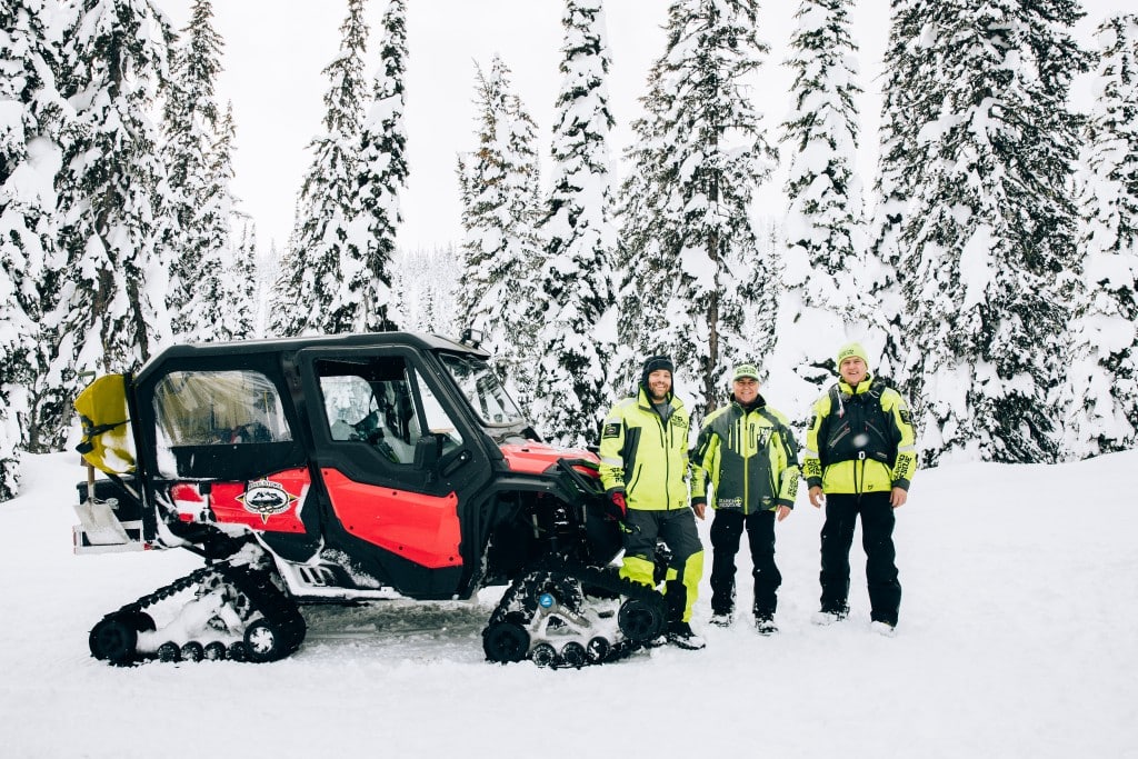 Revelstoke Snowmobile Club Groomer with three operators standing in front of in on one of the trails Revelstoke Snowmobile Club maintains.