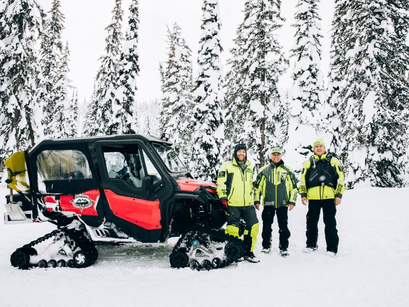 Revelstoke Snowmobile Club Groomer with three operators standing in front of in on one of the trails Revelstoke Snowmobile Club maintains.