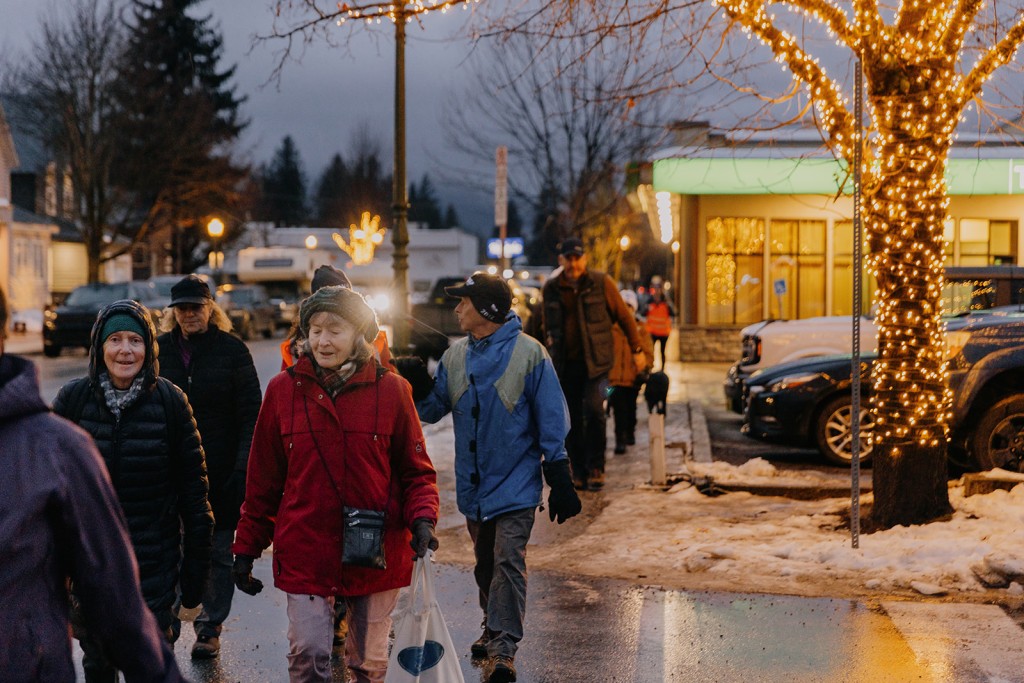 Revelstoke Coldest Night of the Year 2025 participants walk along a wet and lit up street, all wearing various styles of winter clothing