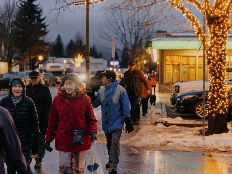 Revelstoke Coldest Night of the Year 2025 participants walk along a wet and lit up street, all wearing various styles of winter clothing