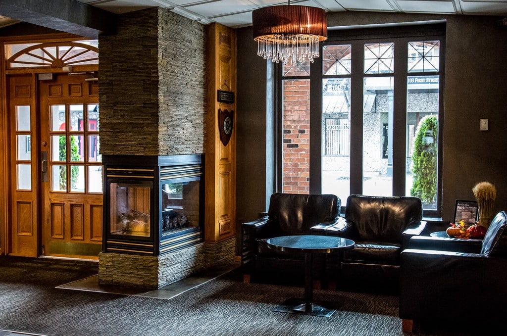 Interior of Revelstoke hotel The Regent. Darker lighting with wood elements and stone walls. Three plush leather-style couches and alarge framed window looking on Revelstoke's main street.