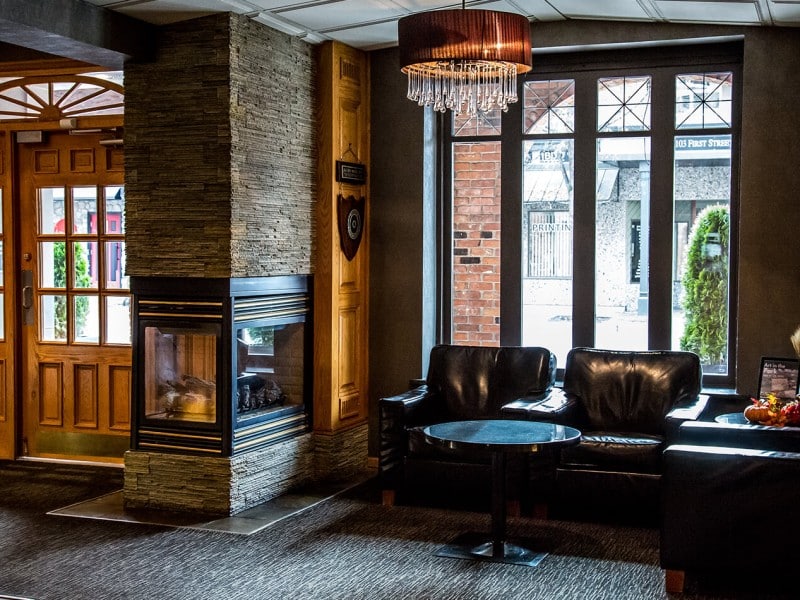 Interior of Revelstoke hotel The Regent. Darker lighting with wood elements and stone walls. Three plush leather-style couches and alarge framed window looking on Revelstoke's main street.