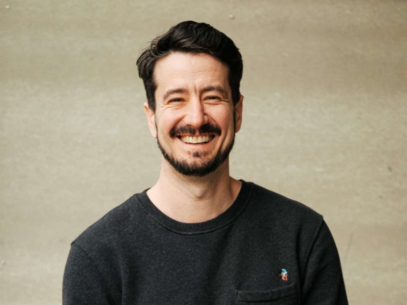 Good Way Homes CEO Logan Ashley, a Cree man with a short haircut and styled beard looking at the camera and smiling wide.