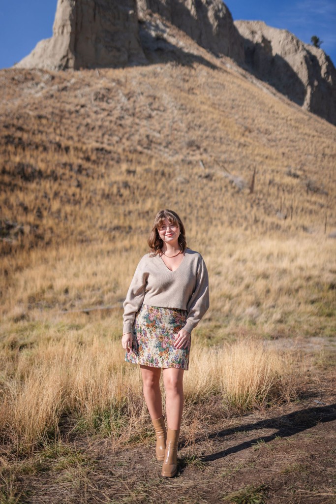 Hollie Ferguson in a sweater and artsy floral print skirt standing in the Kamloops hoodoos.
