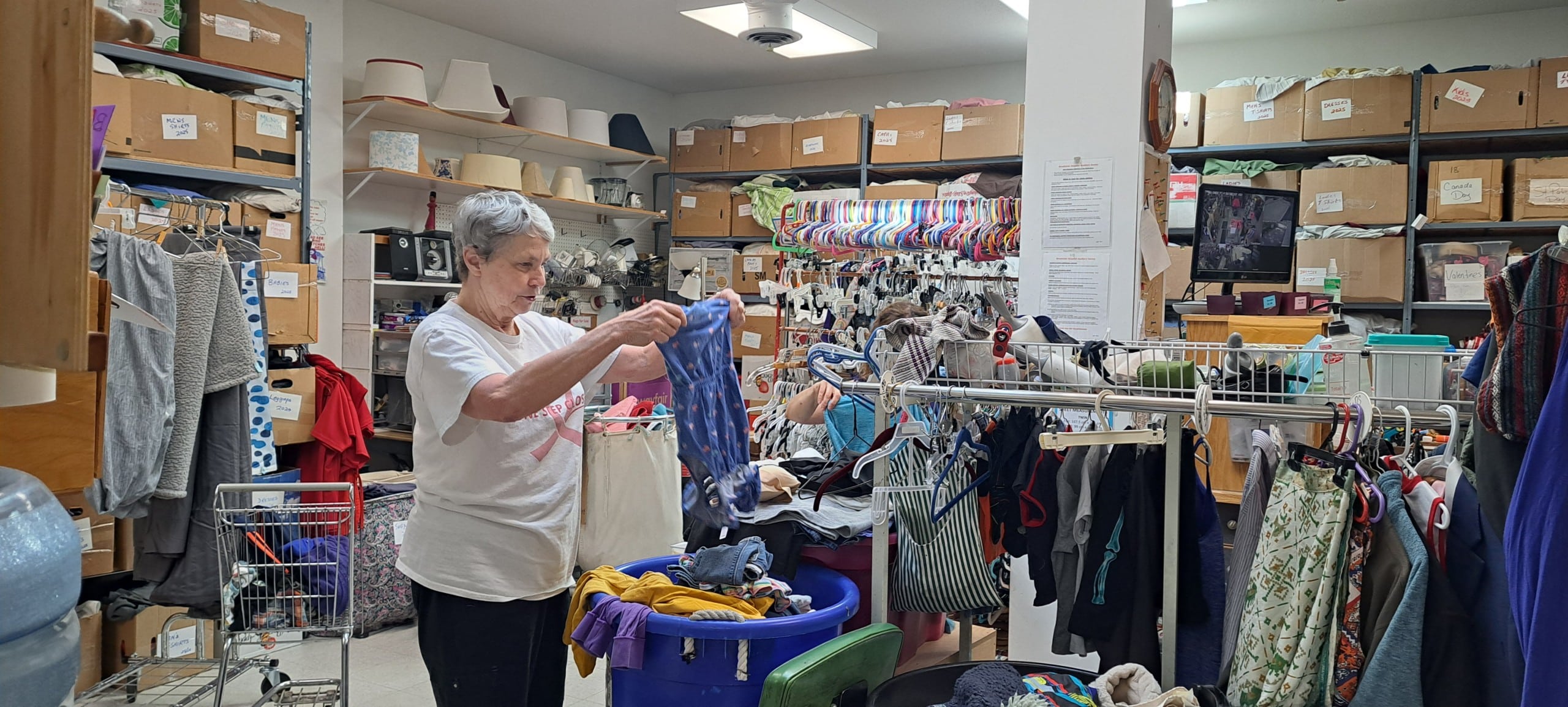 Cathy Thacker works through boxes of clothing recently donated to the Revelstoke Thrift Store. She is holding up a purple children's dress to make sure there are no rips, stains or missing parts.