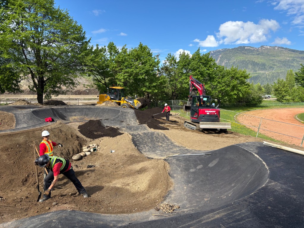 construction workers in an open field working on a pavement track that slopes into two different bends.