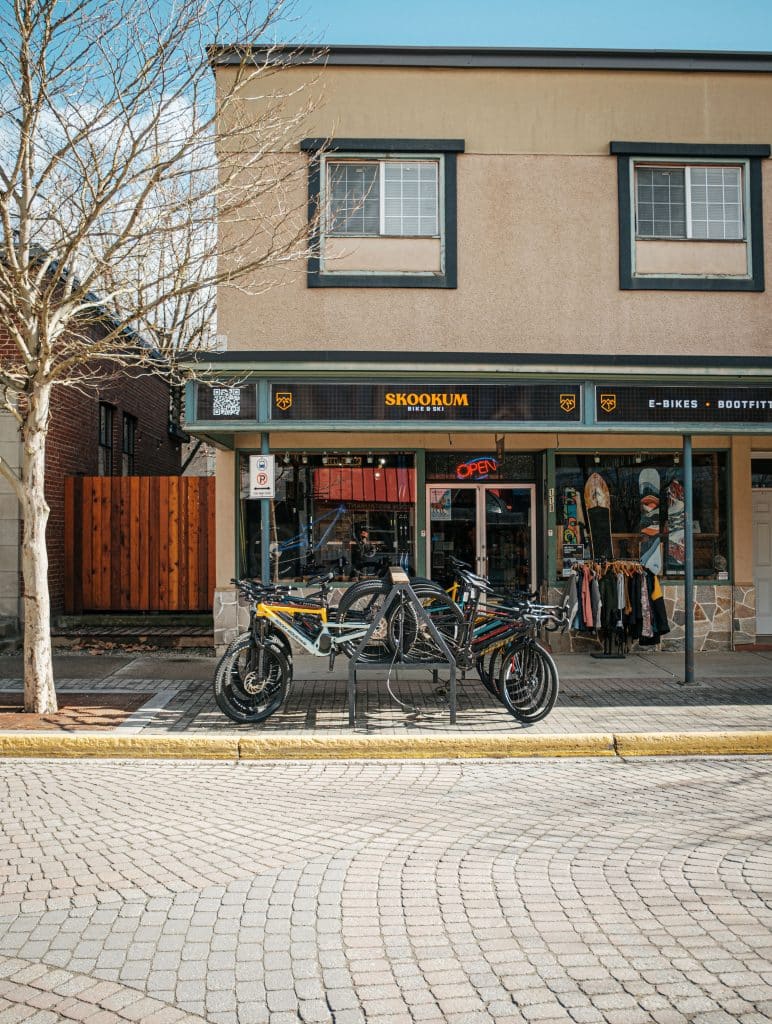 Skookum, one of the bike shops in Revelstoke exterior shot with a rack of bikes outside the large glass window.