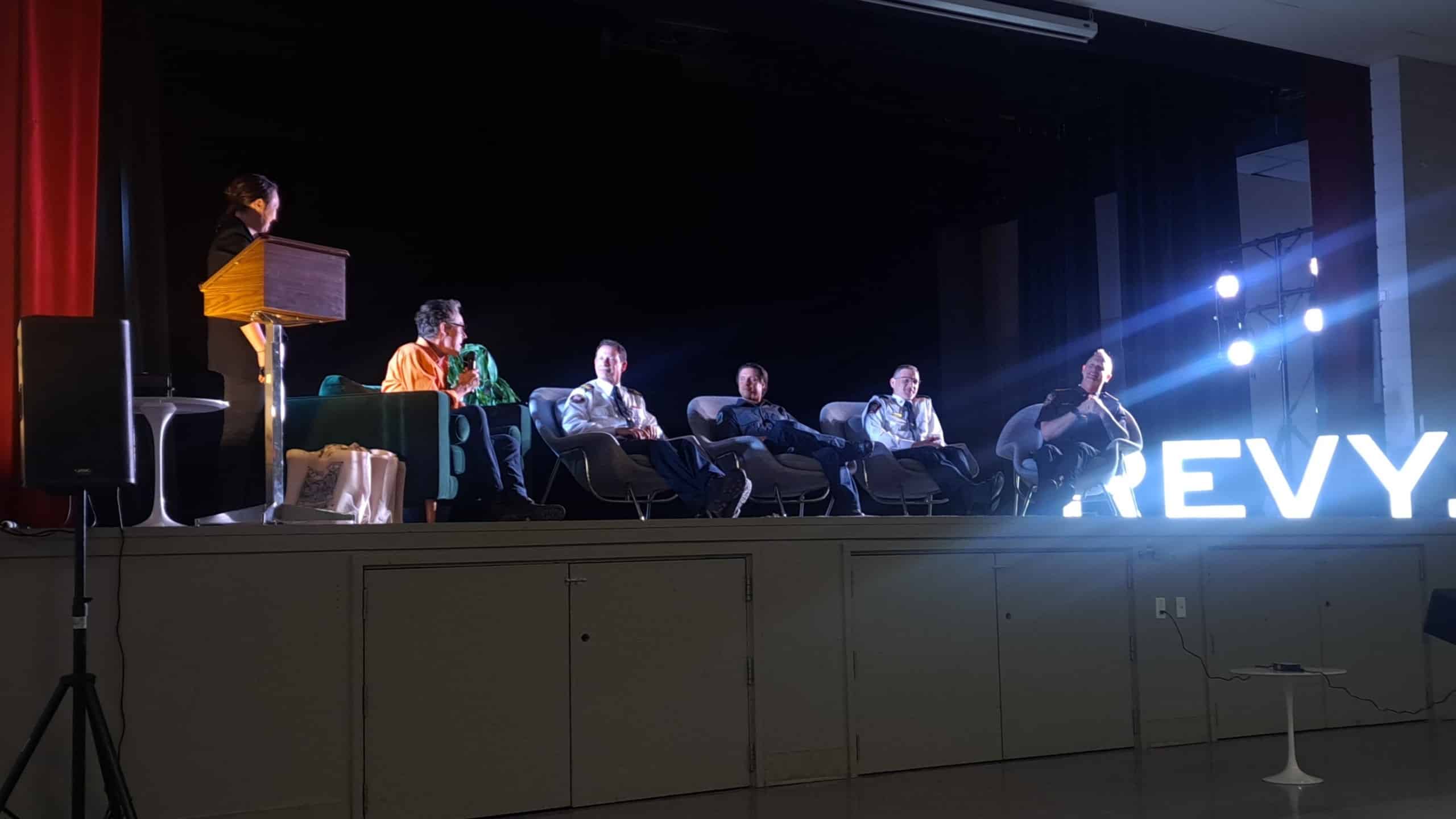 FireSmart panel sitting on a stage in a line, all holding microphones as they talk to the office.