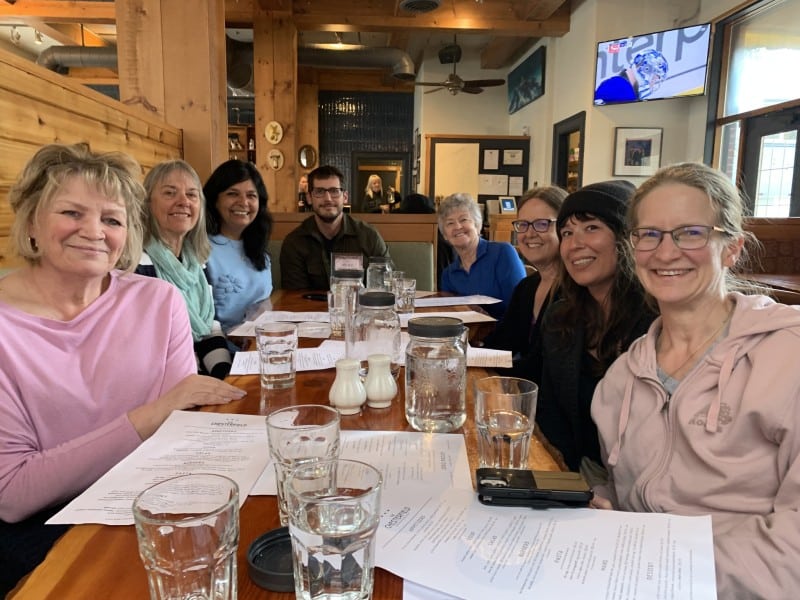 Revelstoke’s Emergency Support Services volunteer team of eight sit around a restaurant table, all looking at the camera and smiling.