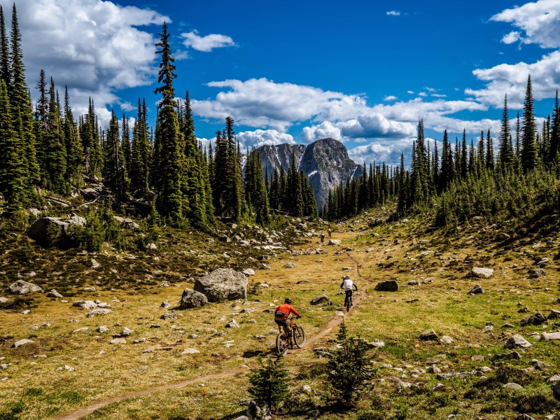 Wandering Wheels tour rider on a dirt trail in a open patch before the trail winds back between the mountain trees.