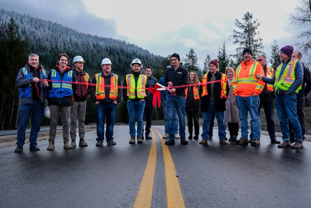 A dozen men in various outdoor and construction gear standing side by side on a newly paved road.