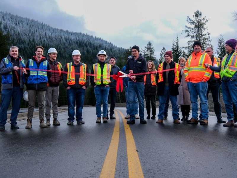 A dozen men in various outdoor and construction gear standing side by side on a newly paved road.