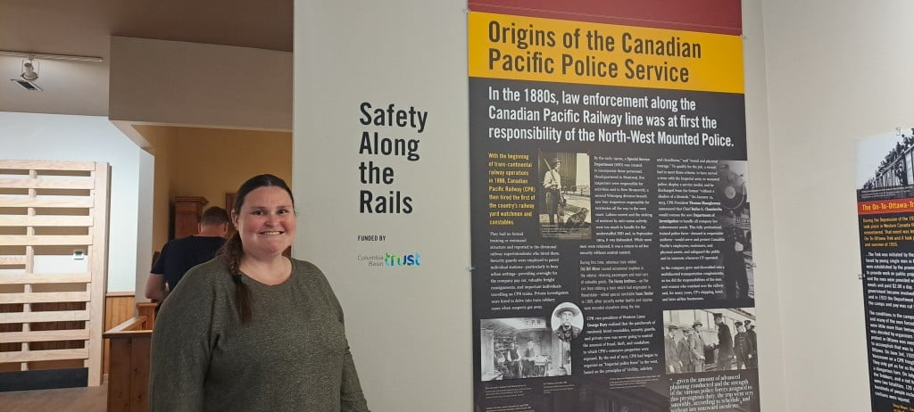 Victoria Hill, woman stands in front of a sign for Safety Along the Rails and an exhibit panel