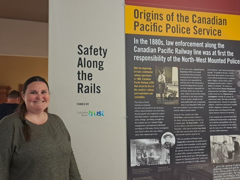 Victoria Hill, woman stands in front of a sign for Safety Along the Rails and an exhibit panel