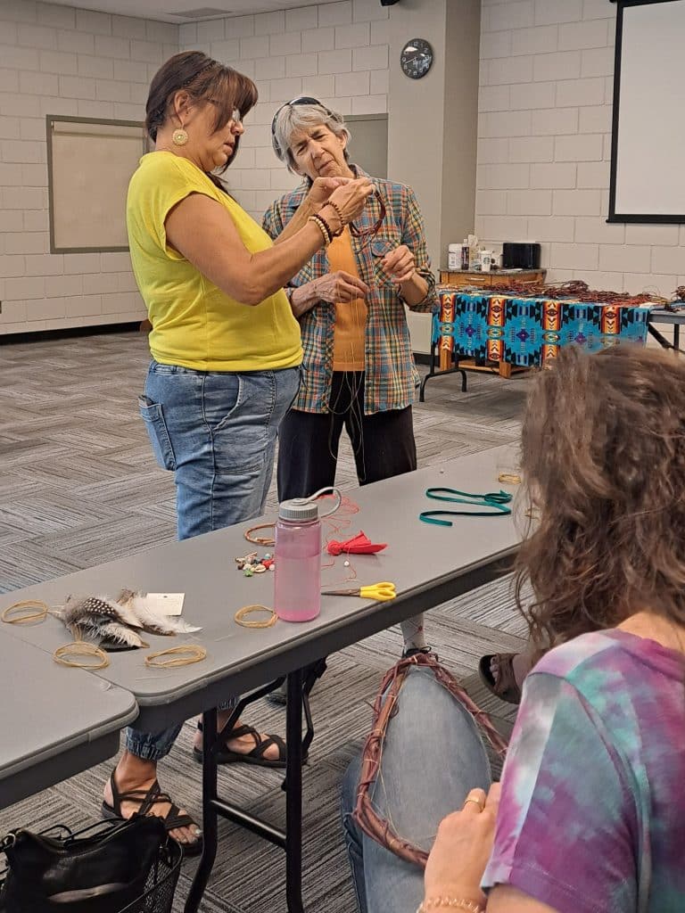 Artist Delrée Dumont and a dreamcatcher class participant looking over the knotwork of a dreamcatcher in progress during Revelstoke's National Indigenous History Month celebrations.
