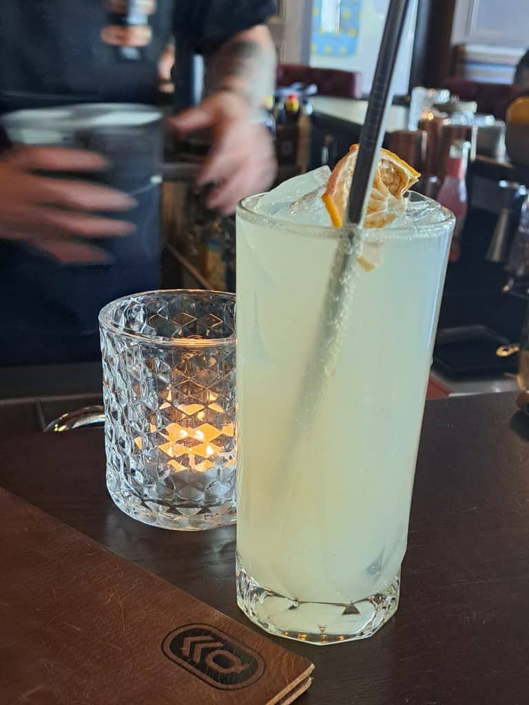 Quartermaster Eatery’s Moscow Mule mocktail, a slightly green tinted drink. A candle behind the drink is illuminating it from the back.