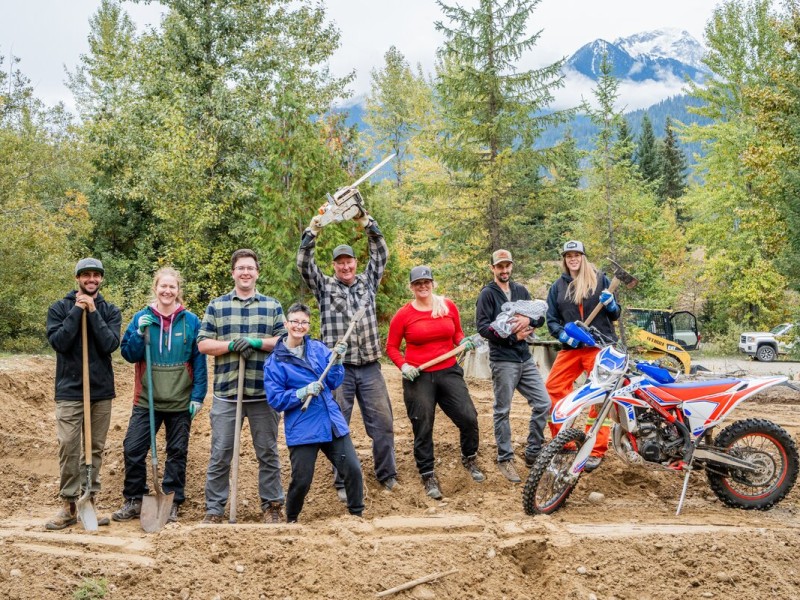 A group of Thanksgiving Back volunteers stand side by side on a large dirt trail, some holding shovels as they look at the camera and smile.