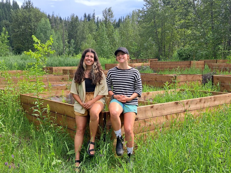 Commons Roots youth program leaders sitting on the edge of a large garden box in a small clearing.