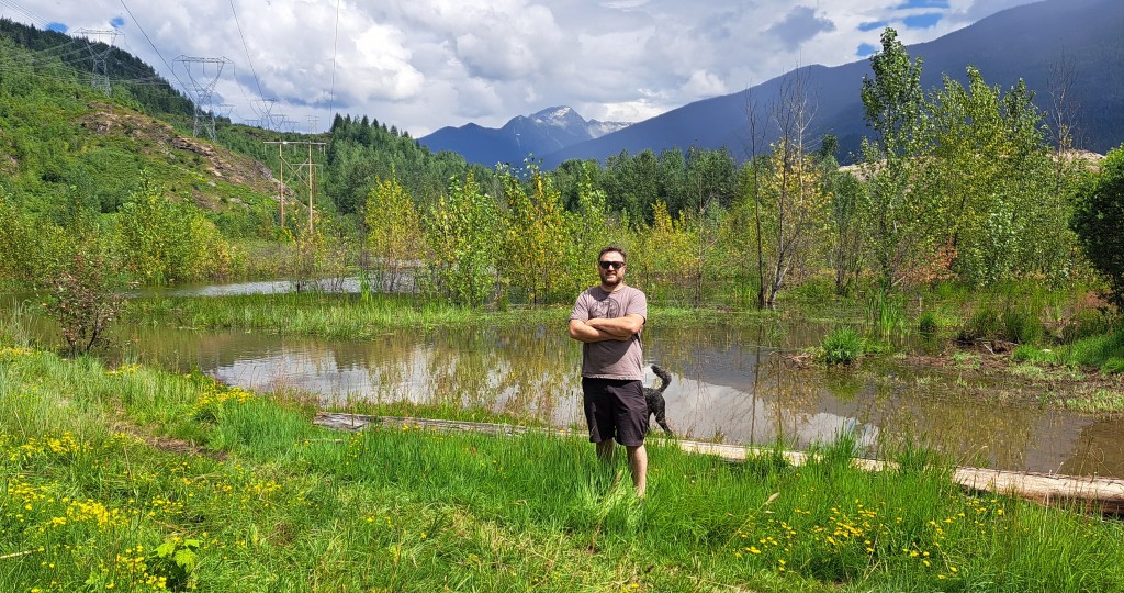 Liam Marshall stand in front of a sizable pond created by an out of frame beaver dam