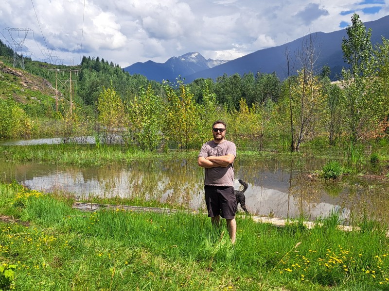 Liam Marshall stand in front of a sizable pond created by an out of frame beaver dam