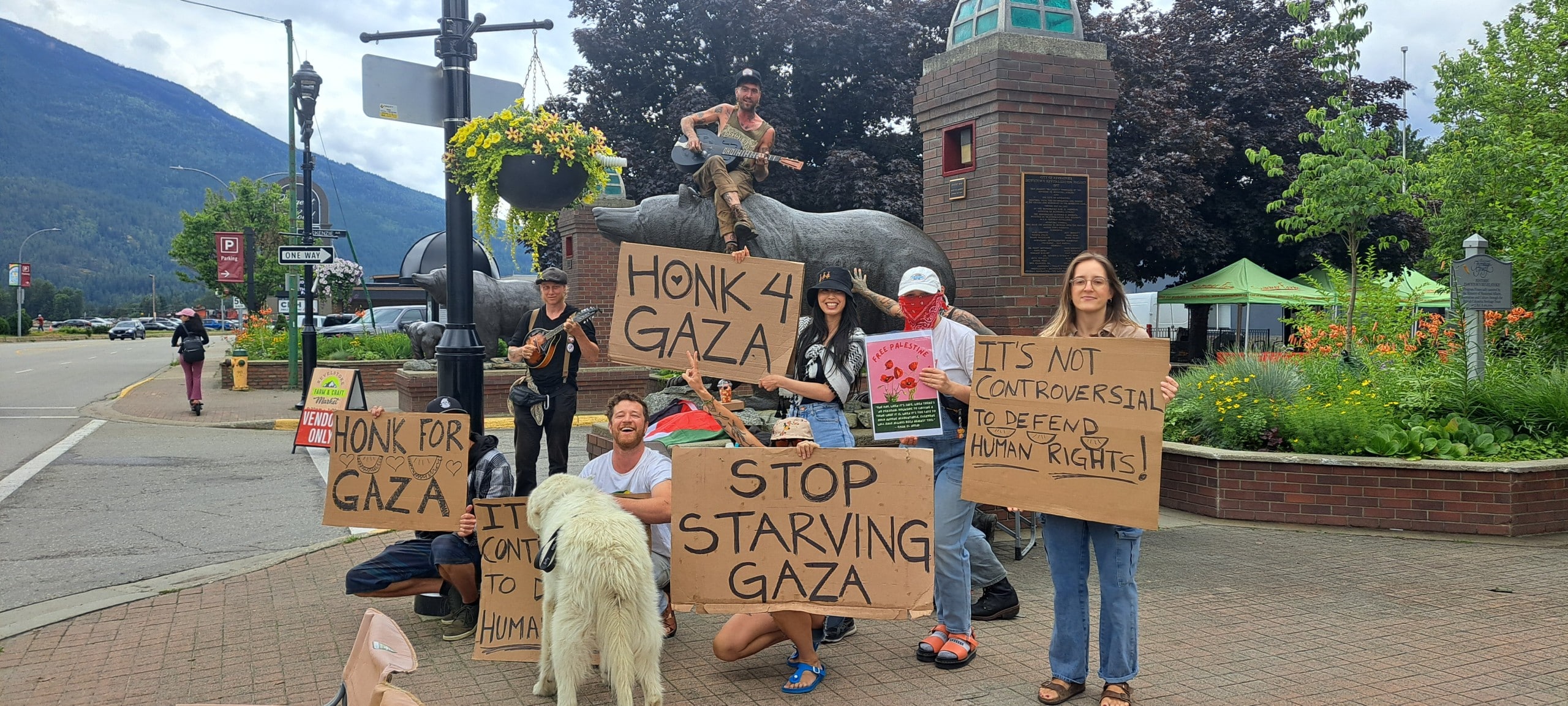 Humanity in Revelstoke supporters standing in front of the Grizzly Plaza bear statue all holding different signs in support of Palestine.