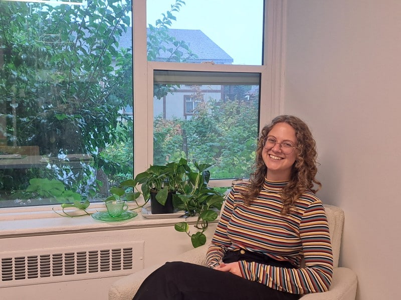 Taylor Sandell, Revelstoke Visual Arts director sitting in a chair in their office.