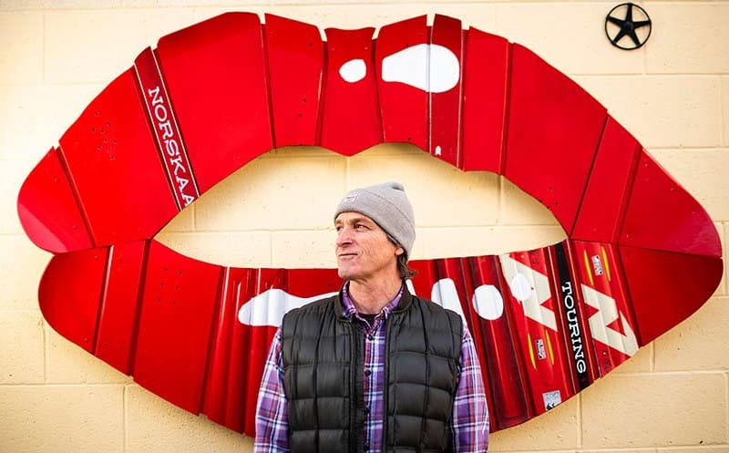Revelstoke Art Alleries Rob Buchanan in front of his piece, a pair of bright red lips built out of old skis and snowboards.