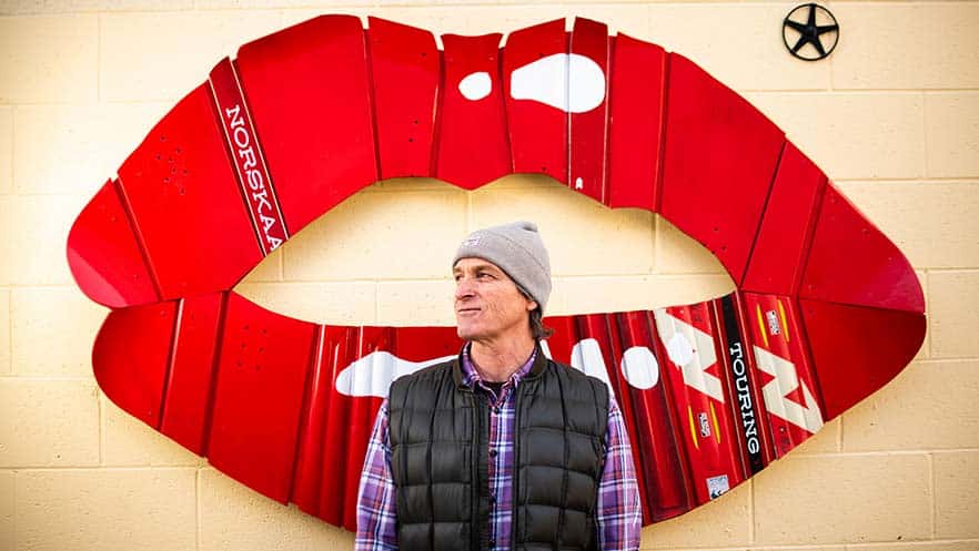 Revelstoke Art Alleries Rob Buchanan in front of his piece, a pair of bright red lips built out of old skis and snowboards.