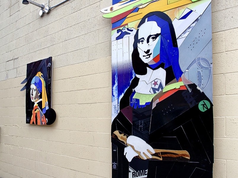 Mock ups of the Mona Lisa and the Girl With the Pearl Earing, made from skis and snowboards. The pieces are hanging from the back wall of a building.