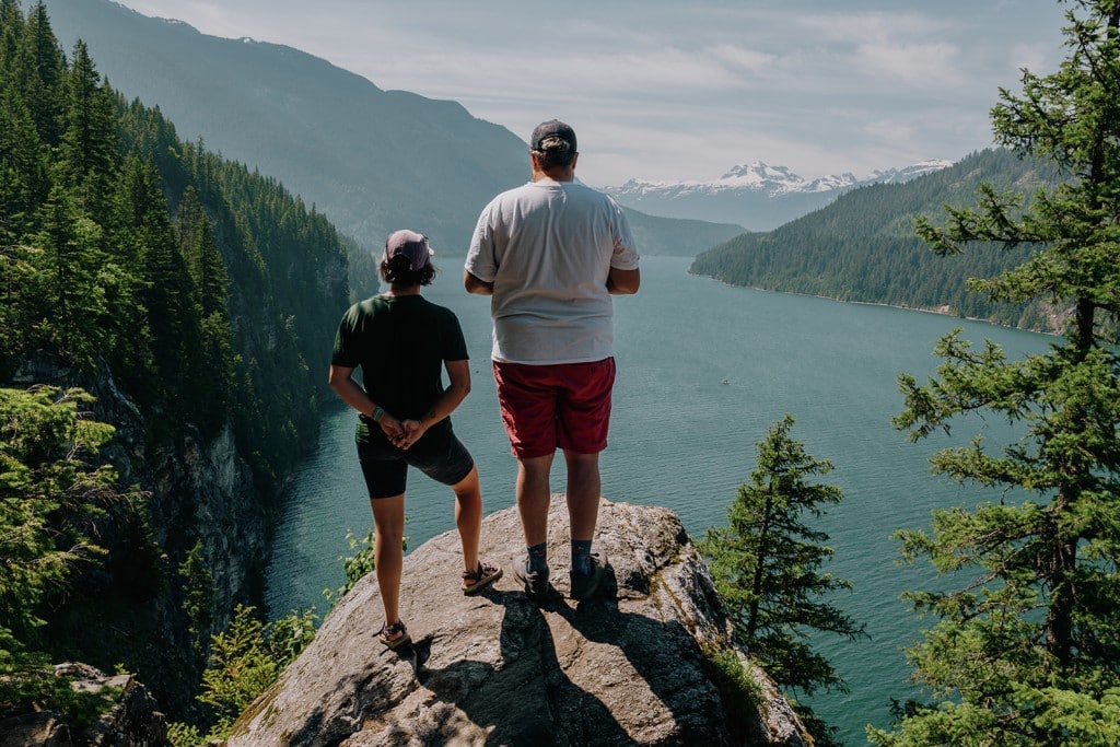 Jade Berrill and Nathan Van Norman with backs to the camera standing on a cliff edge looking out onto the Columbia River