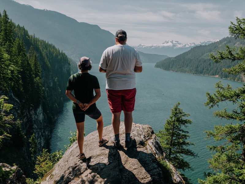 Jade Berrill and Nathan Van Norman with backs to the camera standing on a cliff edge looking out onto the Columbia River