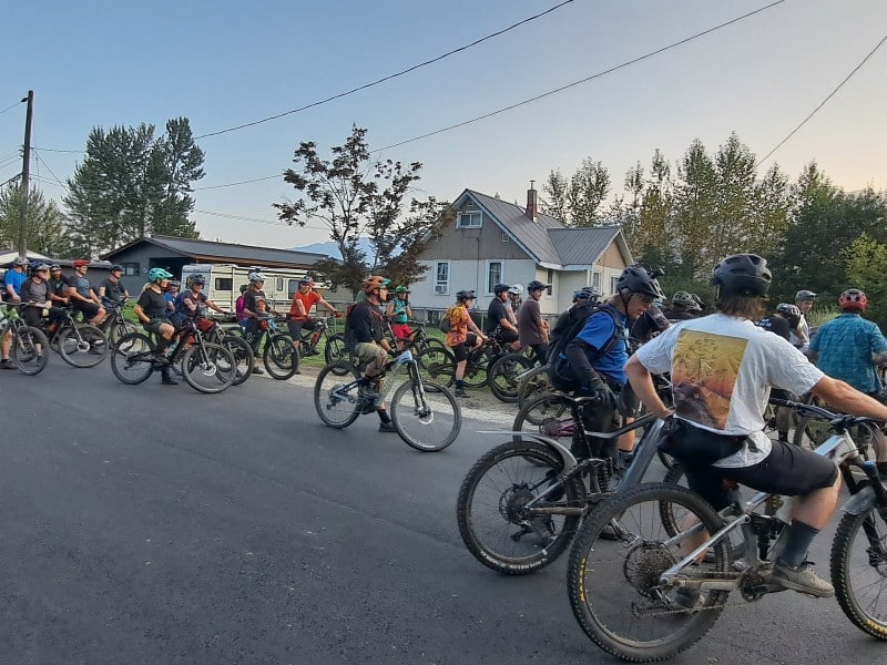 Pedal and Pint's 50 cyclists on mountain bikes all gathering at an intersection in front of Revelstoke's Big Eddy Bridge.