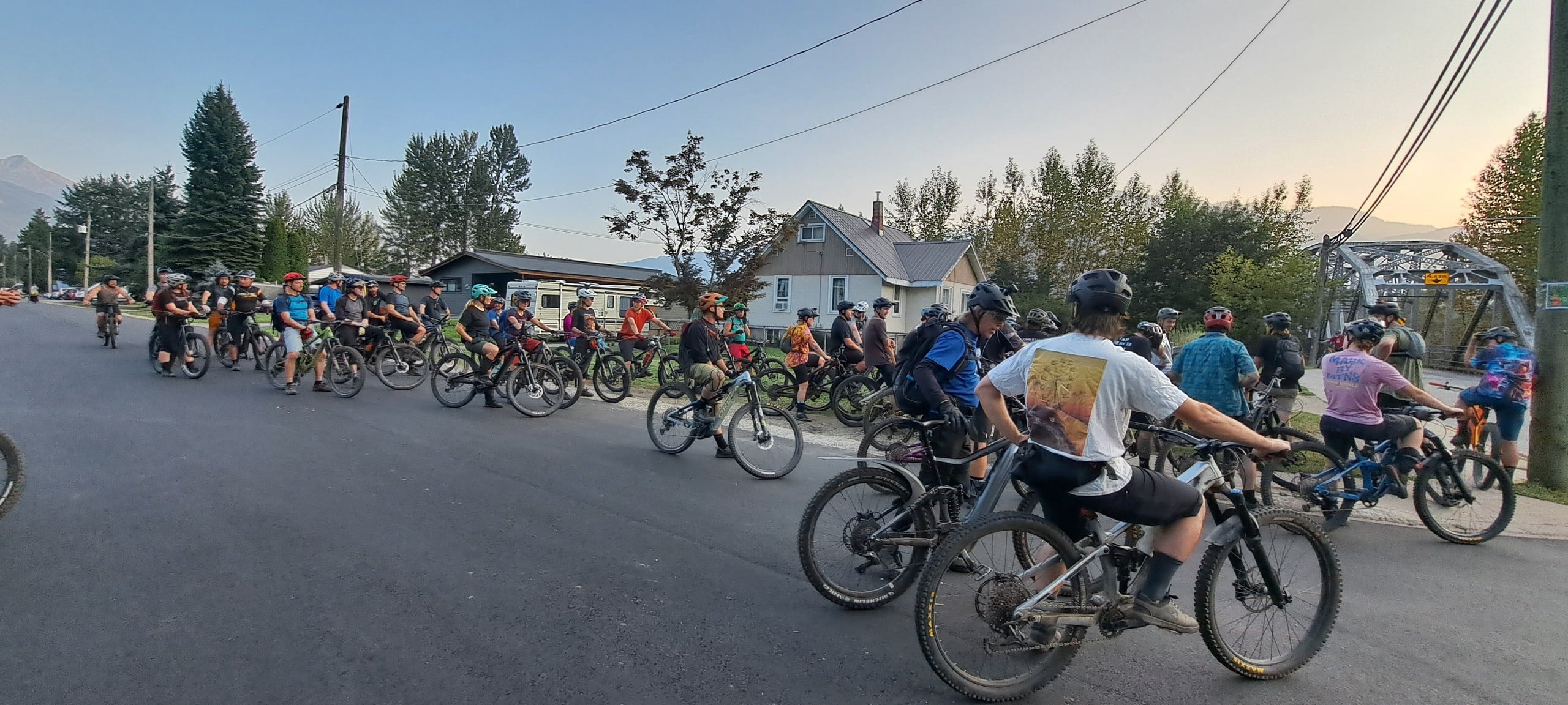 Pedal and Pint's 50 cyclists on mountain bikes all gathering at an intersection in front of Revelstoke's Big Eddy Bridge.