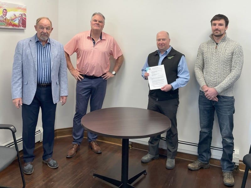 A group of white men standing around a table and smiling at the camera, one of them holding the Revy Own home land agreement
