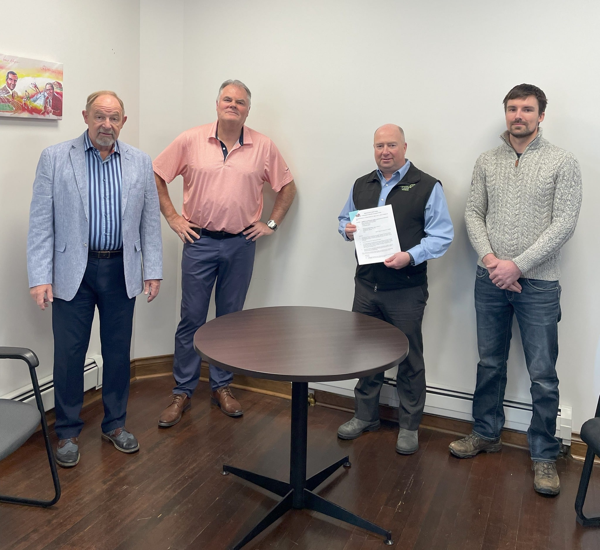 A group of white men standing around a table and smiling at the camera, one of them holding the Revy Own home land agreement